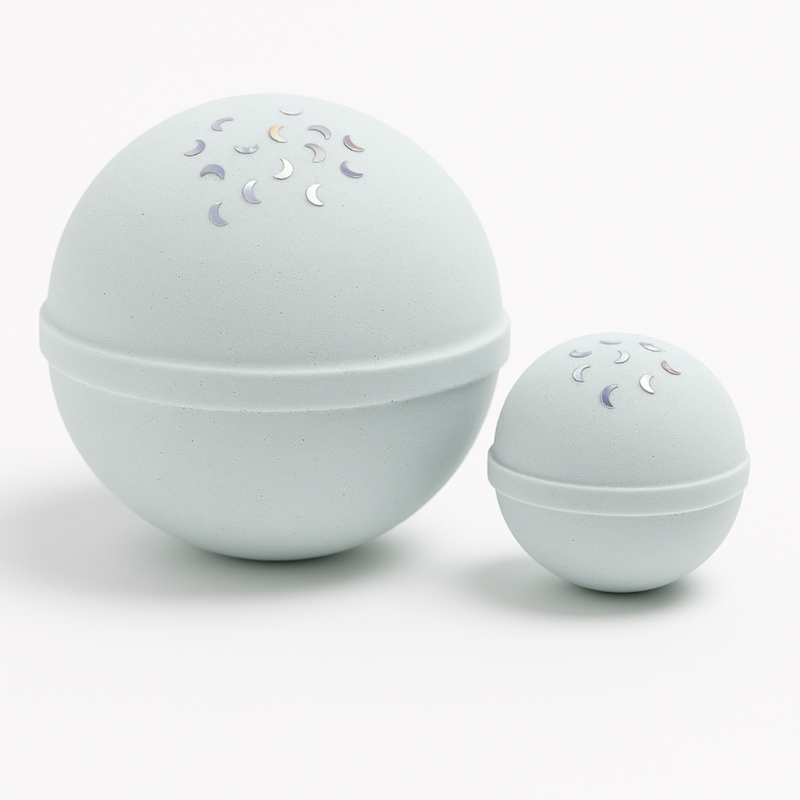 Two white spherical bath bombs with decorative elements on a light gray background