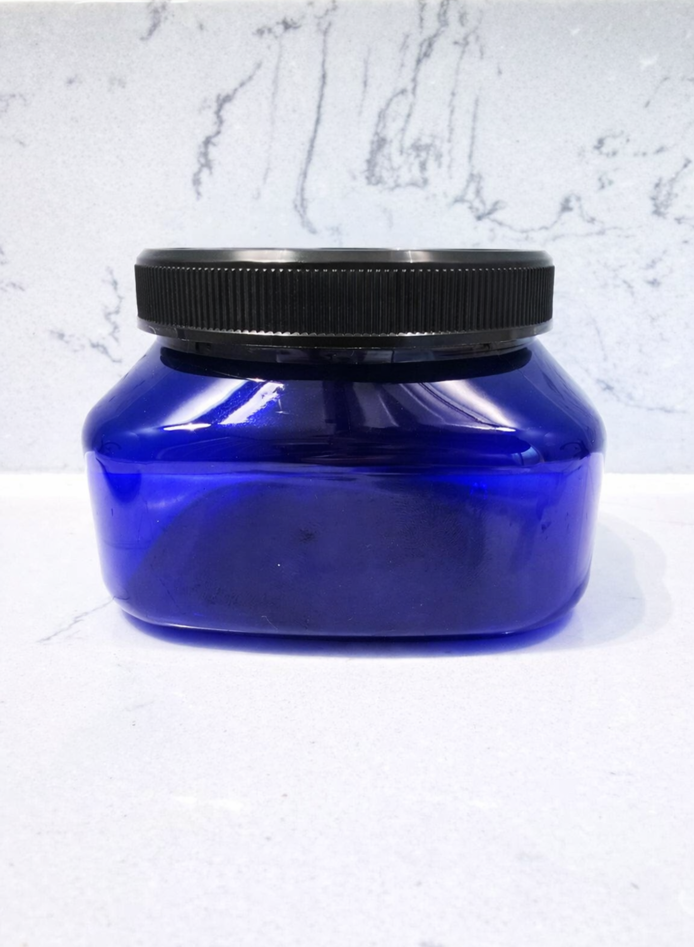 Blue container with black lid on a white marble background