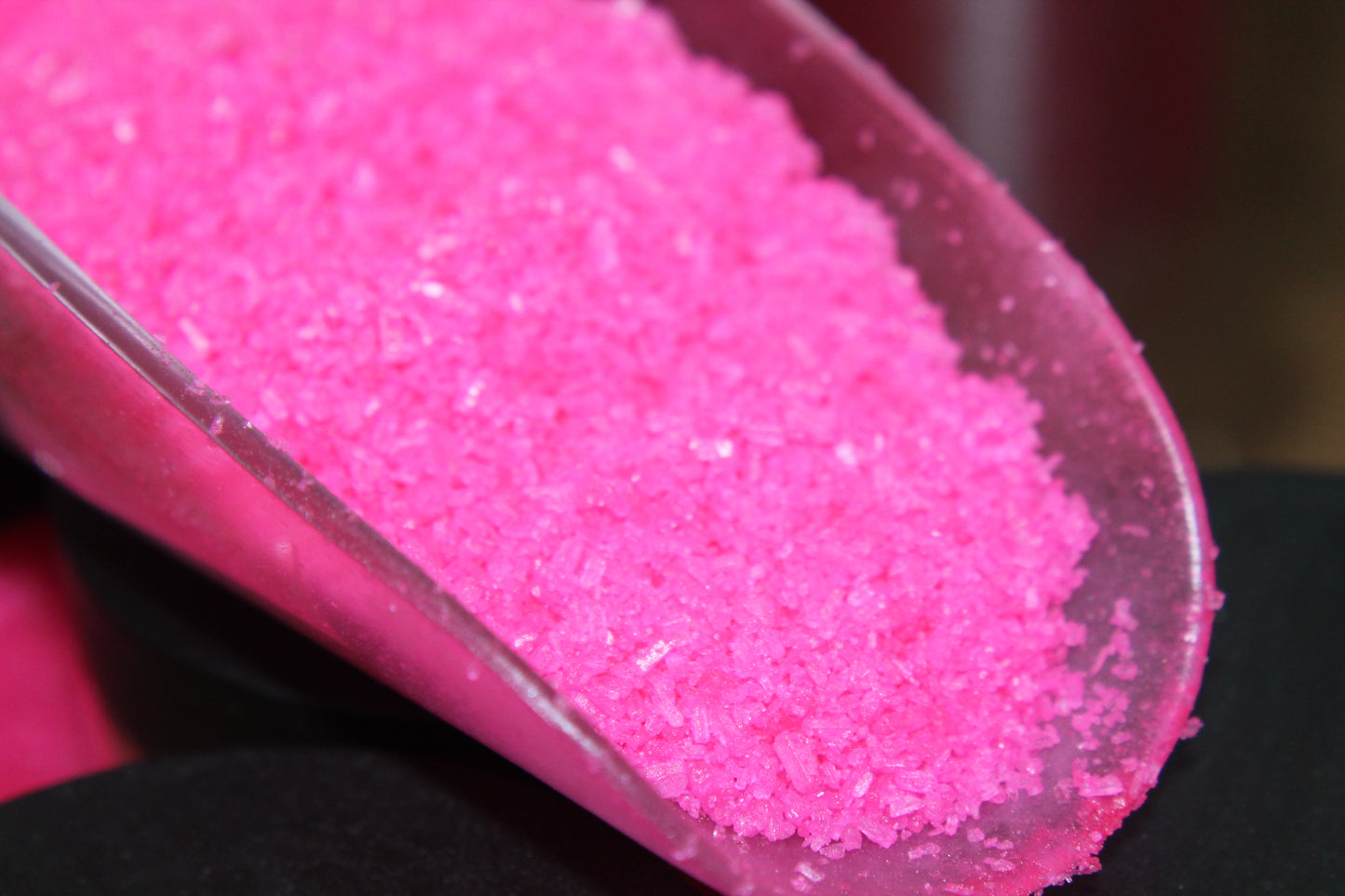 Close-up of pink bath salt in a clear scoop with a blurred background