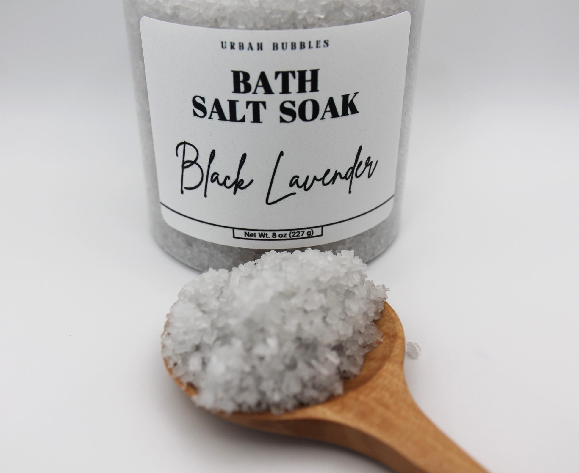 Bath salt soak labeled 'Black Lavender' with a wooden spoonful of salt on a white background