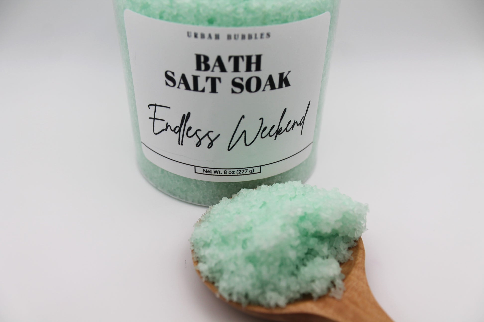 Bath salt soak with a wooden spoonful of green bath salts on a white background