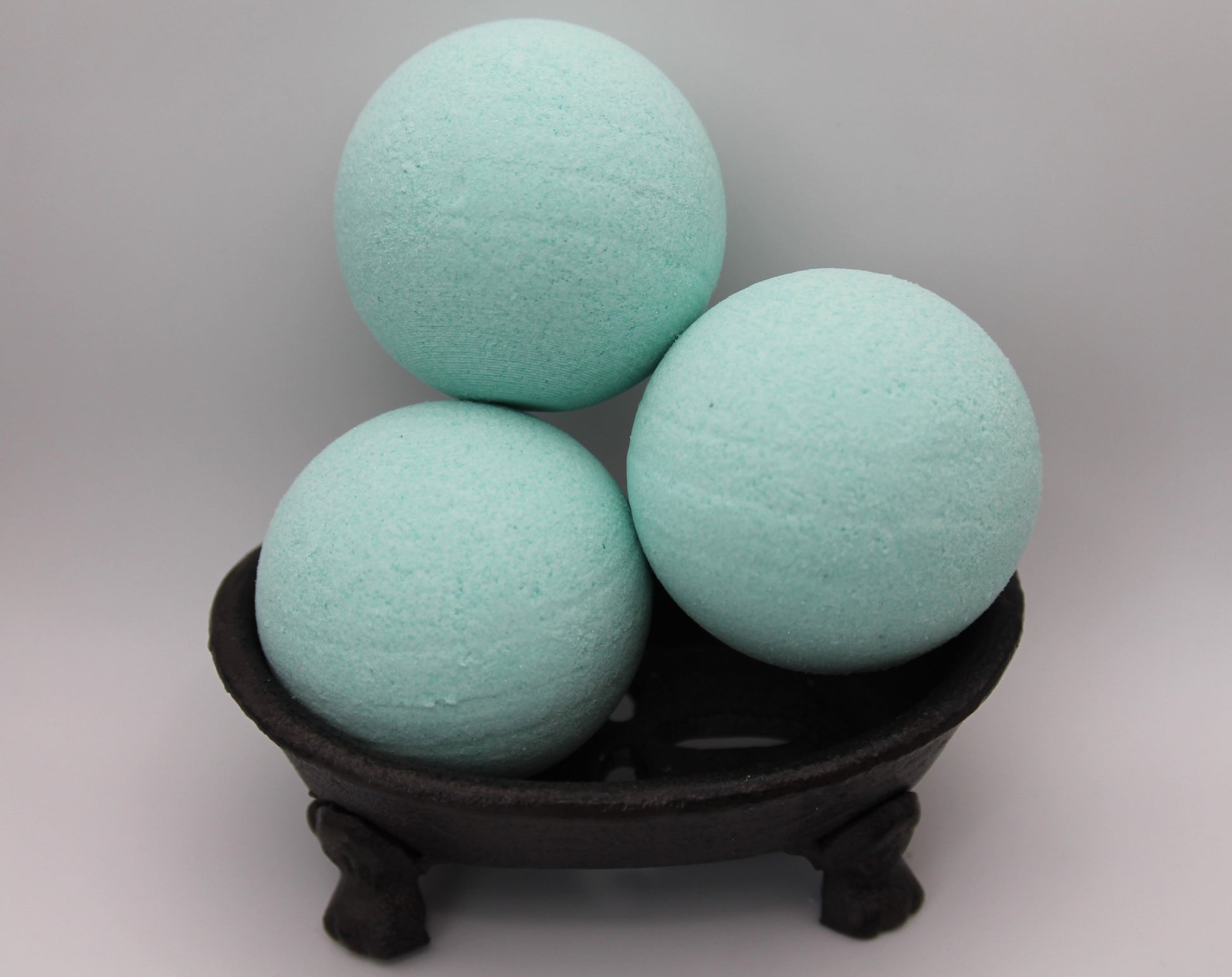 Three light blue bath bombs on a dark stand against a gray background