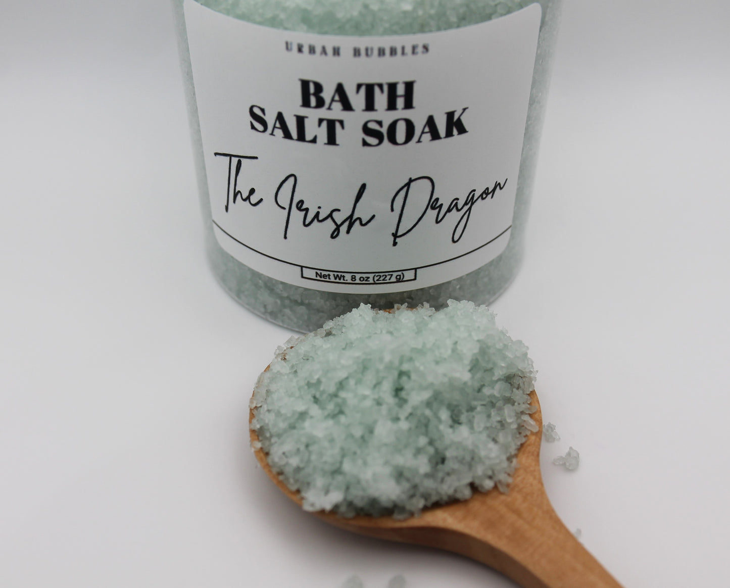 Bath salt soak with a wooden spoonful of green salt on a white background