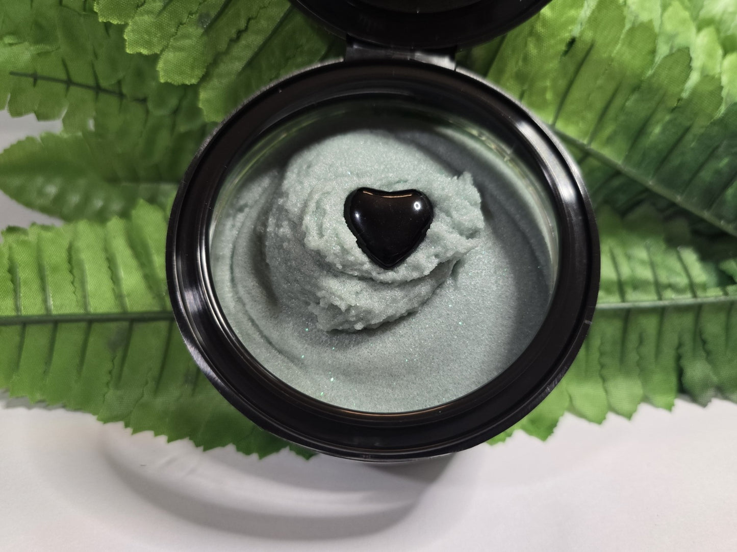Jar of green cream with a heart-shaped object on a leafy background