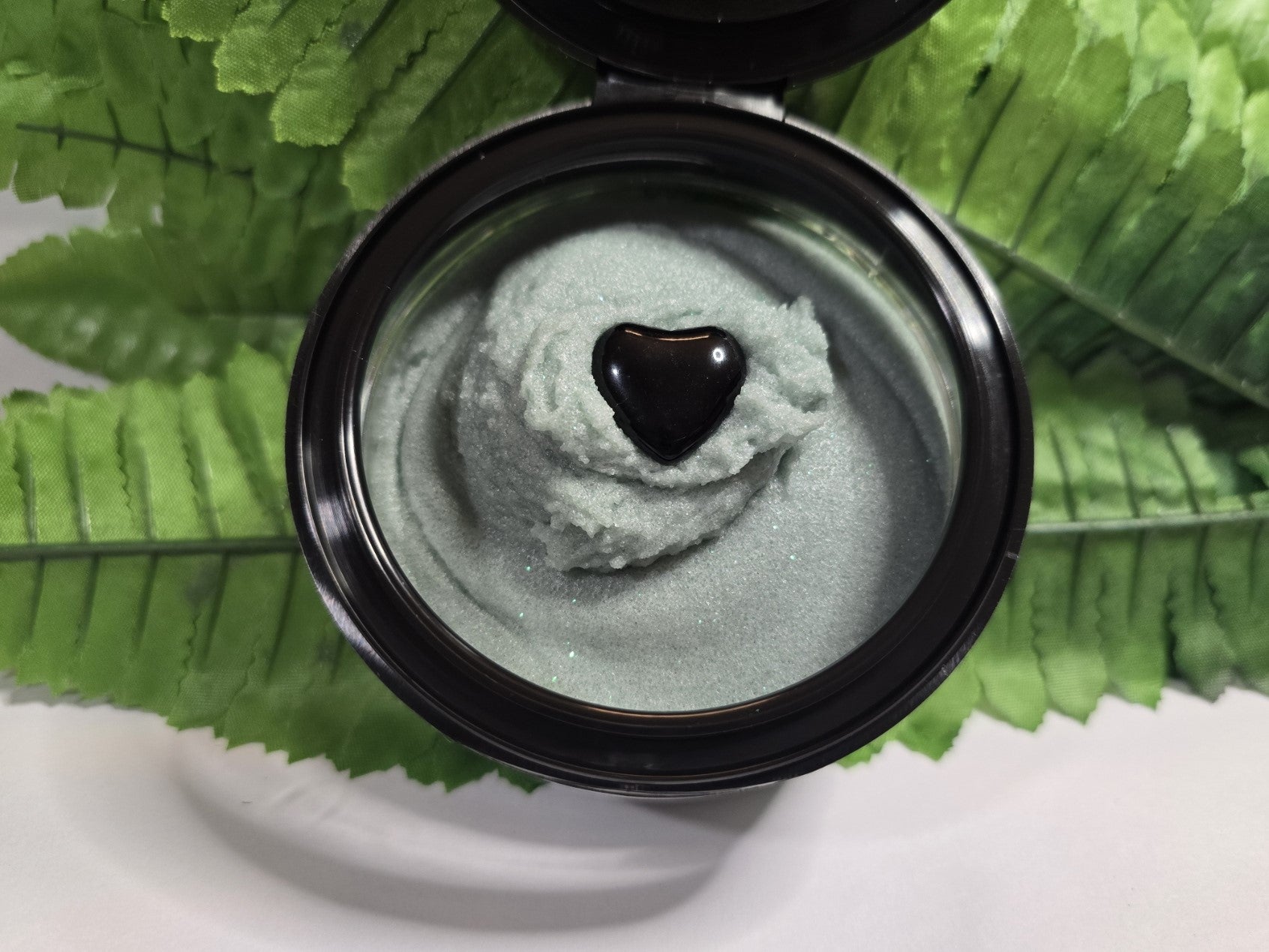 Jar of green cream with a heart-shaped object on a leafy background