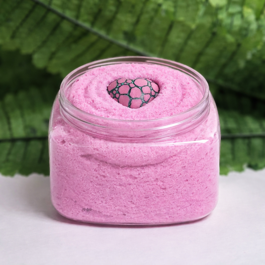 Pink sugar scrub in jar with green foliage in the background
