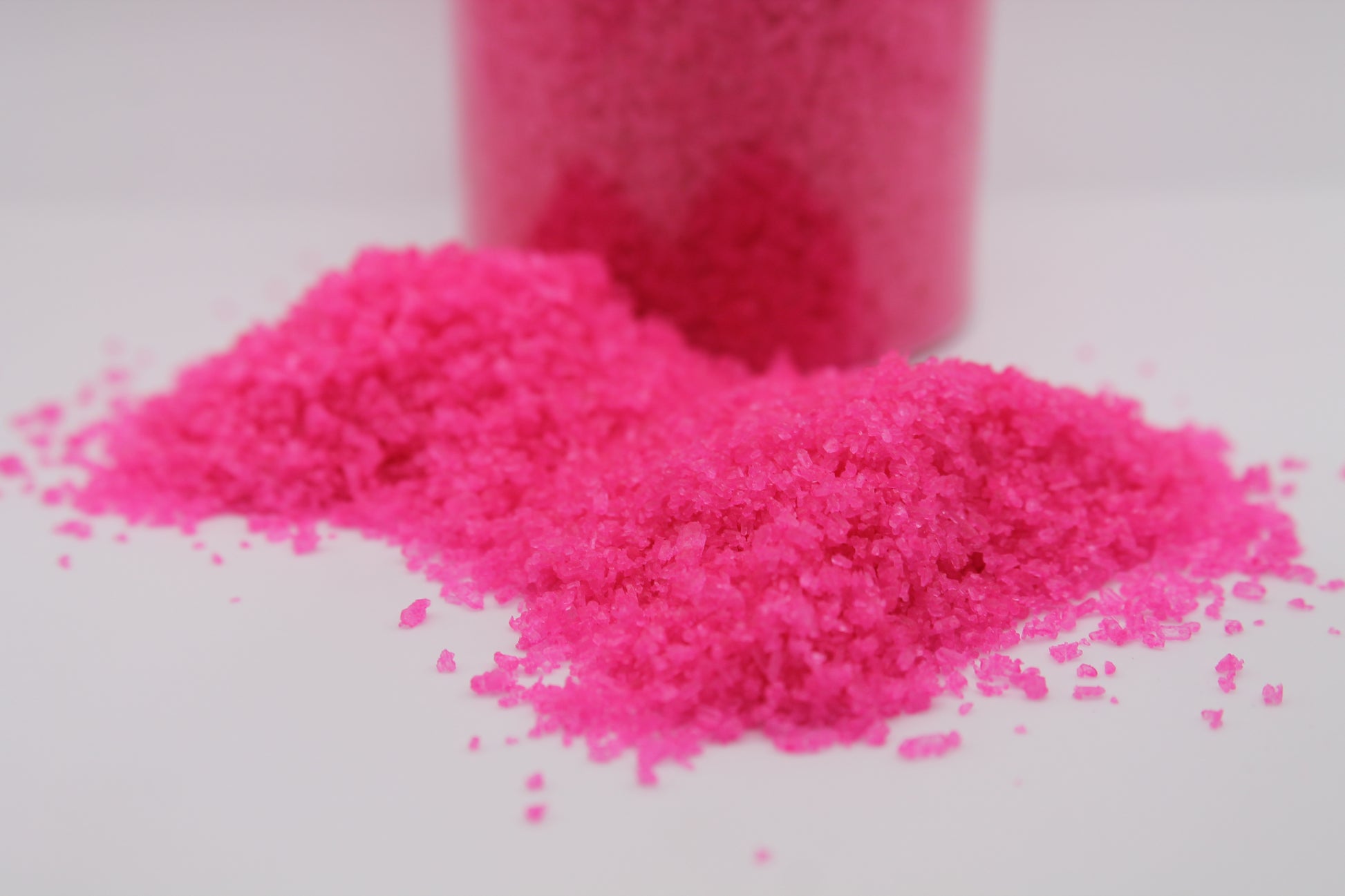 Pink bath salt container in the background on a white surface
