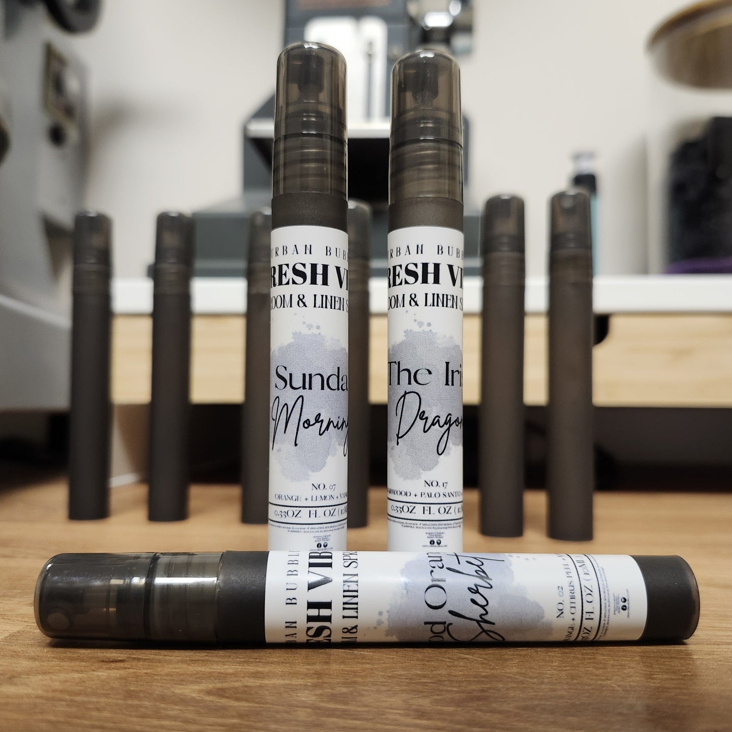 Three travel room and linen spray bottles with visible labels on a wooden surface